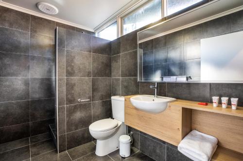 een badkamer met een toilet, een wastafel en een spiegel bij Nightcap at Monash Hotel in Clayton North