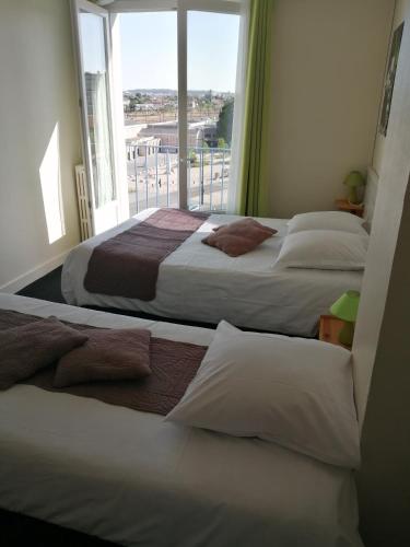 two beds in a room with a large window at Hotel d'Orléans in Angoulême