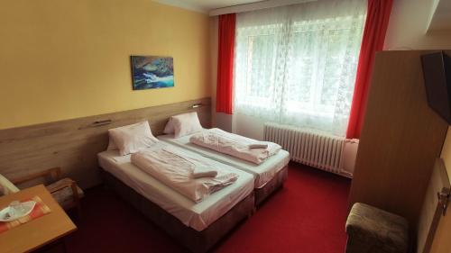 Hotel U Přehrady في Morávka: غرفة نوم بسريرين ونافذة ذات ستائر حمراء