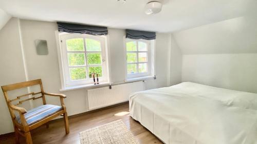 ein Schlafzimmer mit einem Bett und einem Stuhl sowie zwei Fenstern in der Unterkunft Ferienwohnung Hochdorfer Garten in Tating