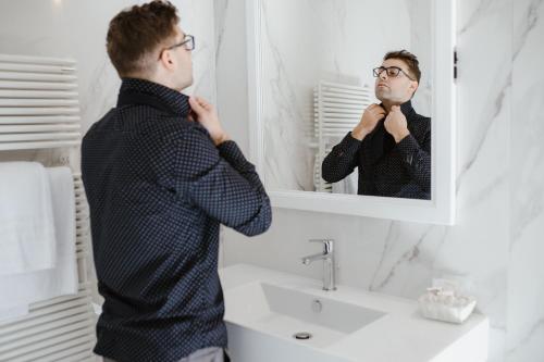 a man adjusting his tie in front of a bathroom mirror at Hotel Città di Parenzo in Trieste