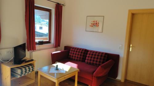 a living room with a red couch and a table at Ferienwohnungen Birnbacher in Sankt Ulrich am Pillersee