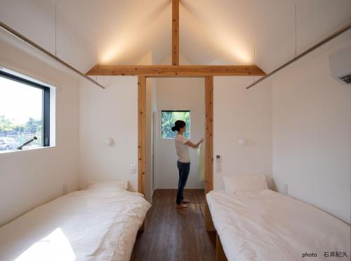 una persona parada en una habitación pequeña con 2 camas en match guest house（まっちゲストハウス）, en Tatsugo