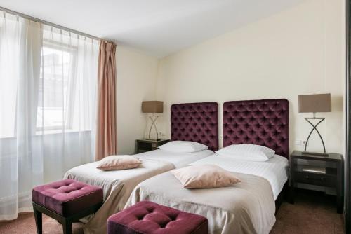 two beds in a hotel room with a purple headboard at Amberton Cathedral Square Hotel Vilnius in Vilnius