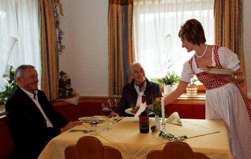 a woman sitting at a table with a woman holding a plate of food at Gasthof-Pension-Kraus in Achslach