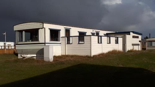 a small white house on a grass field at AMELAND - Ballum: Stacaravan Chalet (incl. fietsen) bij strand en zee in Ballum