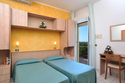 a bedroom with two beds and a desk and a window at Hotel Ausonia in Milano Marittima