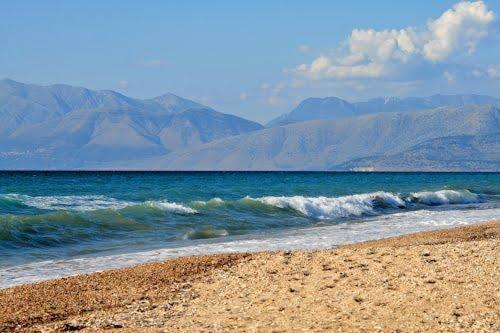 a beach with mountains in the background with waves in the ocean at ARETOUSA APARTMENT in Anapaftíria