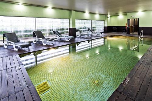 a pool in a building with chairs and a swimming pool at Golden Tulip São João da Madeira in São João da Madeira