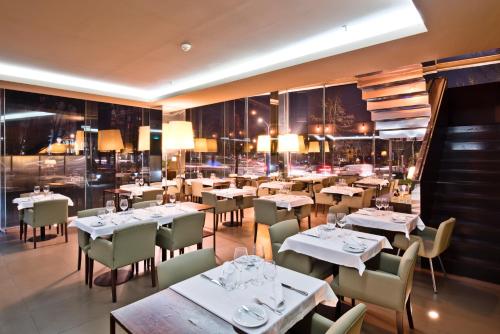 a restaurant with white tables and chairs and windows at Golden Tulip São João da Madeira in São João da Madeira