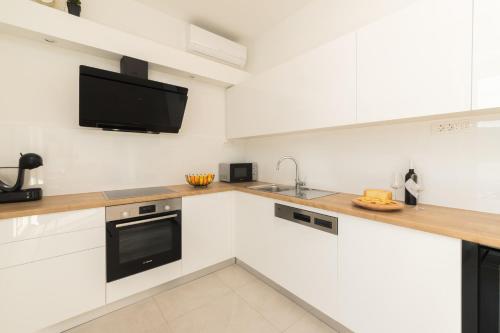 a kitchen with white cabinets and a tv on the wall at Villa Belveder in Pag