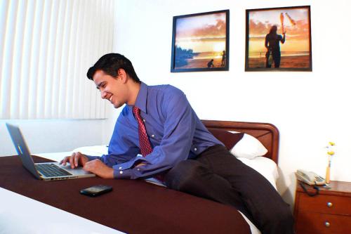 a man sitting on a bed using a laptop computer at Hotel Castell - Cerca Del Aeropuerto in Guayaquil