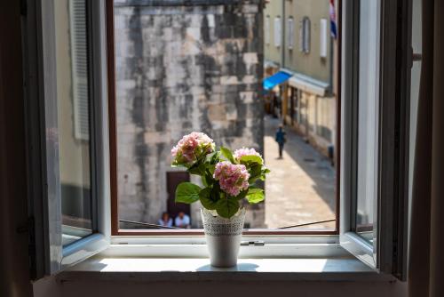 a vase with pink flowers sitting on a window sill at Luxury rooms Zadar old town in Zadar
