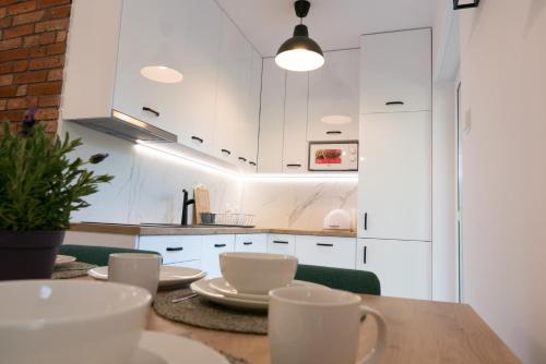 a kitchen with white cabinets and a wooden table with cups at Apartt99 Łeba in Łeba