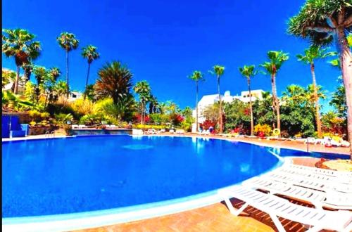una grande piscina con sedie bianche e palme di Eldorado Casa Gi a Playa de las Americas