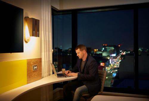 a man sitting at a desk with a laptop in front of a window at Holiday Inn Express Adelaide City Centre by IHG in Adelaide