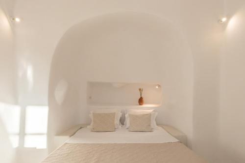 a white bedroom with a bed with two pillows at White Cellar cave houses by Cycladica in Oia