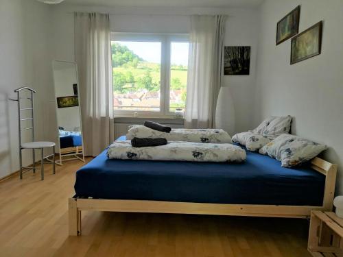 Schlafzimmer mit einem Bett mit blauer Bettwäsche und einem Fenster in der Unterkunft Ferienwohnung "Burgpanorama" in der Südpfalz in Leinsweiler