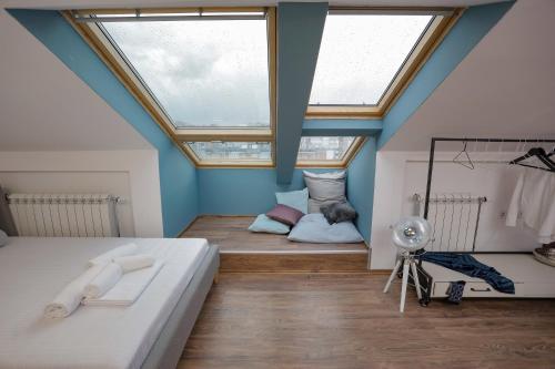 a attic bedroom with a bed and two windows at Different Apartments in Niš