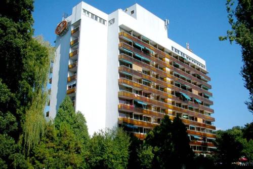 ein hohes weißes Gebäude mit Bäumen davor in der Unterkunft Neptun Apartman in Balatonföldvár
