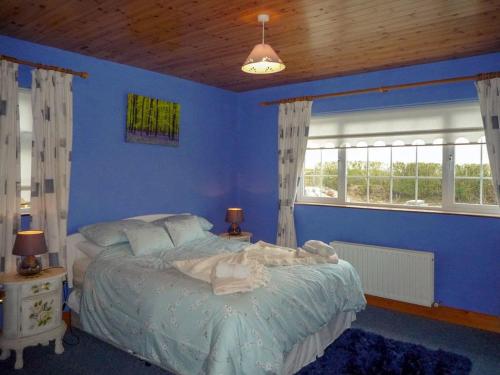 a blue bedroom with a bed and two windows at Ballyheigue Guesthouse in Heirhill