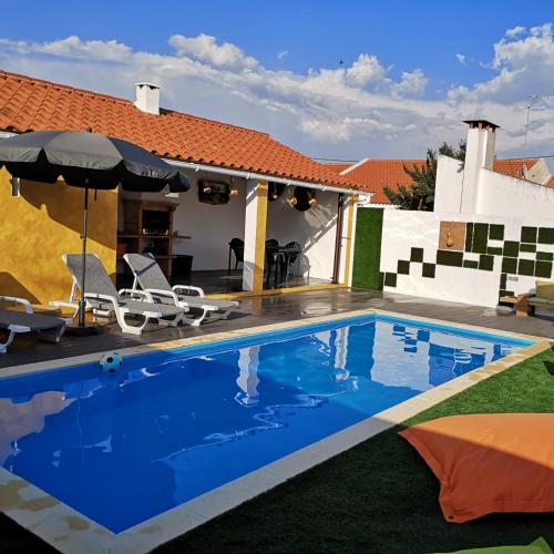 a pool with chairs and an umbrella next to a house at Casinhas do Canário in Montoito