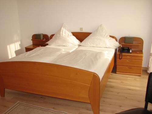ein großes Holzbett mit weißer Bettwäsche und Kissen in der Unterkunft Gasthaus zur Traube in Winterrieden