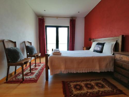 a bedroom with a bed with red walls and two chairs at Gerês e Cabreira - Casa Alexandrina Vilar in Frades