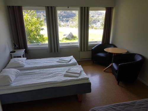 a bedroom with two beds and two chairs and two windows at Folgefonn Gjestetun in Jondal