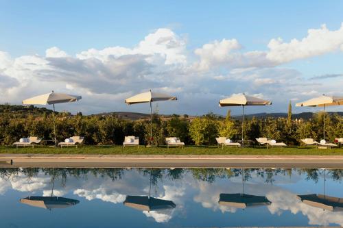 a pool with white umbrellas and chairs and a sky at Locanda Rossa in Capalbio
