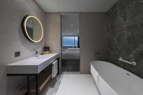 a bathroom with a sink and a tub and a mirror at Golden Tulip FAB Hotel New Taipei in Tamsui
