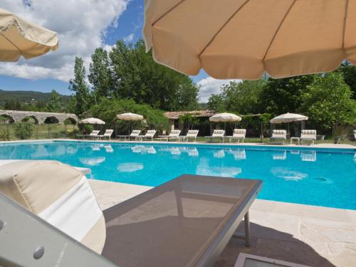 a large swimming pool with chairs and an umbrella at Hotel-Restaurant Le Moulin De La Camandoule in Fayence