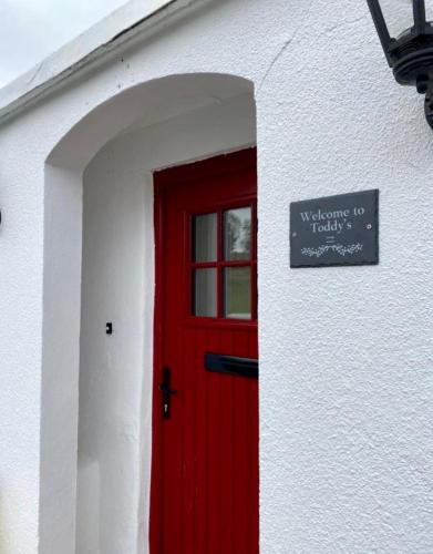 a red door on a white building with a sign on it at Toddys Cottage & Stables in Cavan