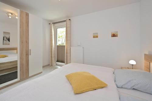 ユリウスルーにあるFerienwohnung Badestrandの白いベッドルーム(黄色い枕付きのベッド付)