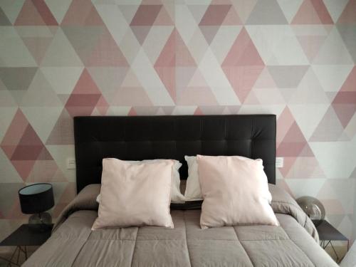 - un lit avec des oreillers blancs dans une chambre avec du papier peint géométrique dans l'établissement Apto la Venta-CON PARKING GRATIS, à Tolède
