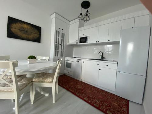 a white kitchen with a table and a white refrigerator at Apartman "Noa" in Sremska Mitrovica