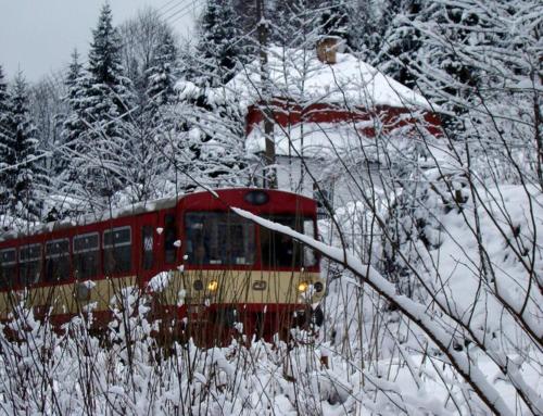 a red and yellow train traveling through a snow covered forest at Penzion "Apartmány U Semušky" in Pernink