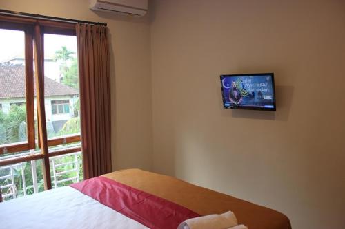 a bedroom with a bed and a tv on the wall at The Sarining Hotel in Tabanan
