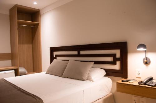 a bedroom with a white bed with a phone and a desk at Mara Turismo Hotel in Catalão