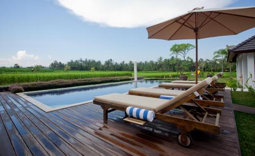 een zwembad met diverse ligstoelen en een parasol bij The Samara Villas & Restaurant in Ubud