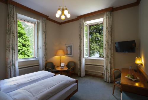 a bedroom with a bed and a desk and two windows at Hotel Le Prese in Poschiavo