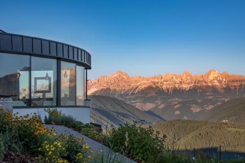 a house on a hill with mountains in the background at Panoramahotel Obkircher in Nova Ponente