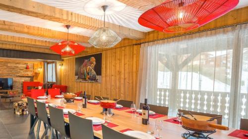 une salle à manger avec une grande table et des lustres rouges dans l'établissement Chante Merle - Chalet - BO Immobilier, à Châtel