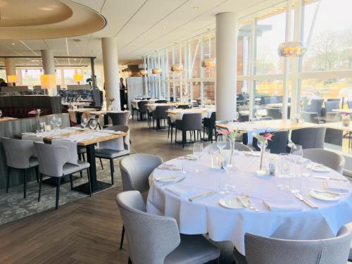 a restaurant with white tables and chairs and windows at Hotel Asteria in Venray