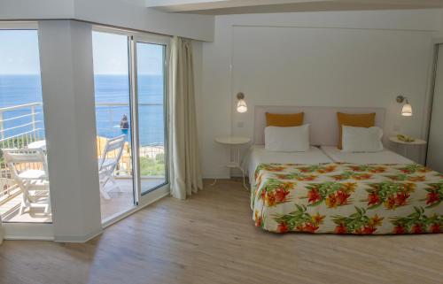 een slaapkamer met een bed en een balkon met uitzicht op de oceaan bij Florasol Residence Hotel - Dorisol hotels in Funchal