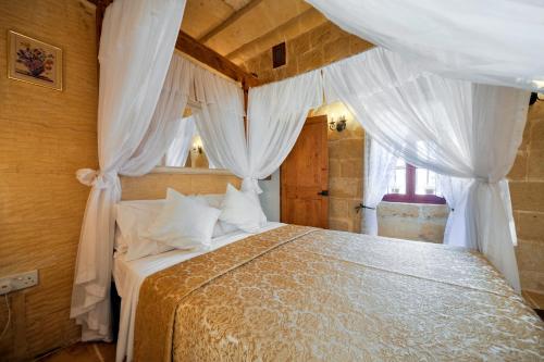 a bedroom with a large bed with white curtains at Tal-Barun Farmhouse in San Lawrenz