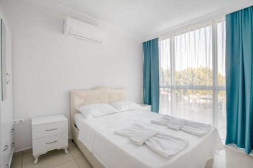 een slaapkamer met een wit bed met blauwe gordijnen en een raam bij Antioch Apart Otel in Didim