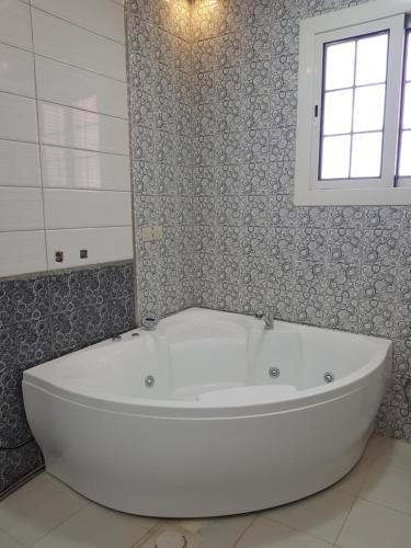 baño con bañera blanca y ventana en منتجع القصر الأبيض, en Unaizah
