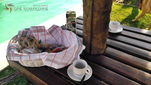 Een mand met eten en kopjes op een houten bank. bij Los Remolinos in Merlo