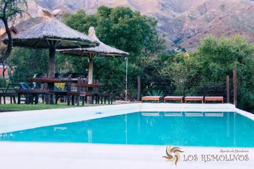 a swimming pool with tables and umbrellas next to a mountain at Los Remolinos in Merlo
